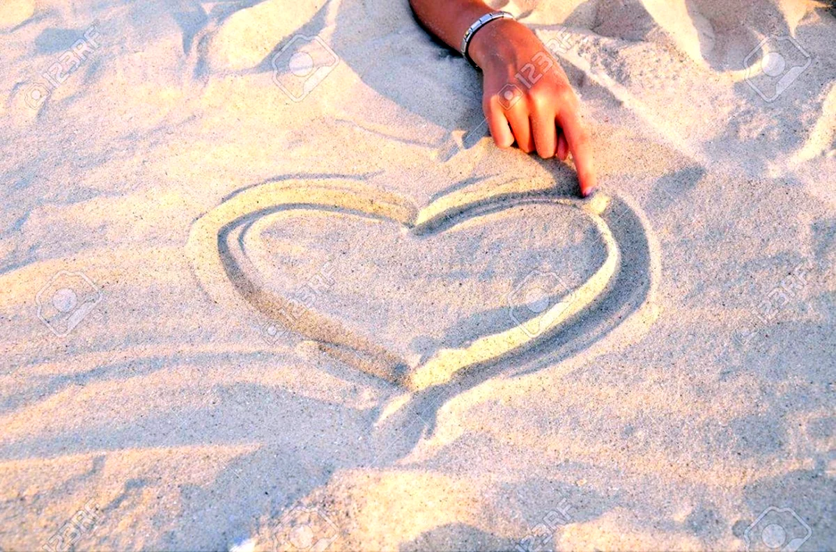 На песке рисует сердце. Красивая картинка