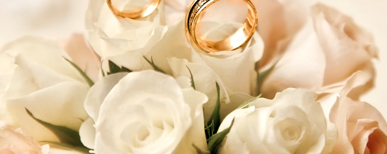 Обручальные кольца на фоне белых роз. Поздравление с годовщиной свадьбы